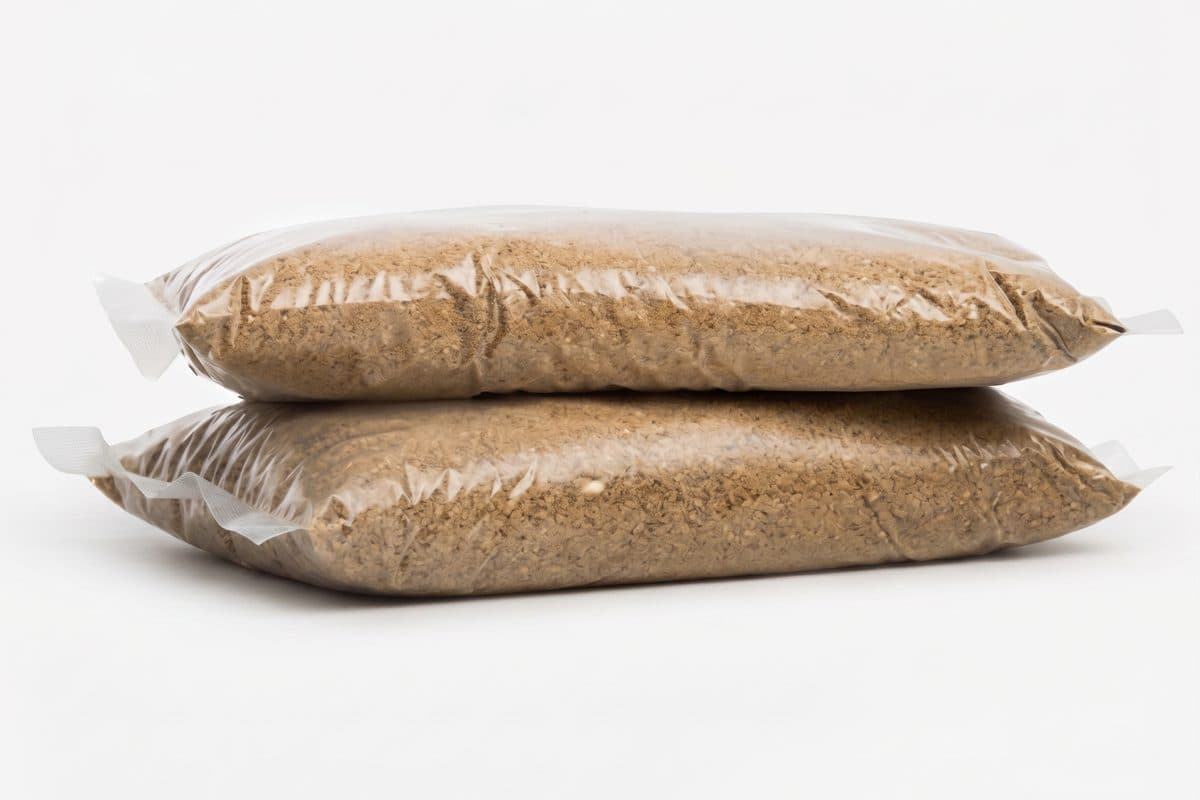 Two sealed transparent packets of dry, brown granular treatment material on a plain background.