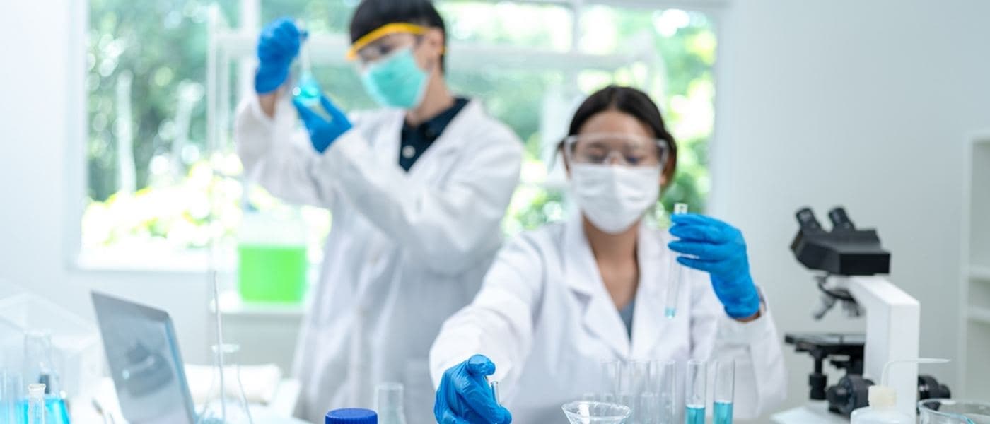 Two scientists in a laboratory examining samples in glass flasks beside a microscope.