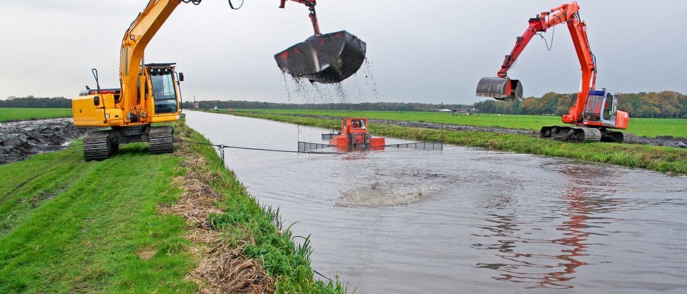 Two long-reach excavators dredging accumulated sediment from a lined canal.