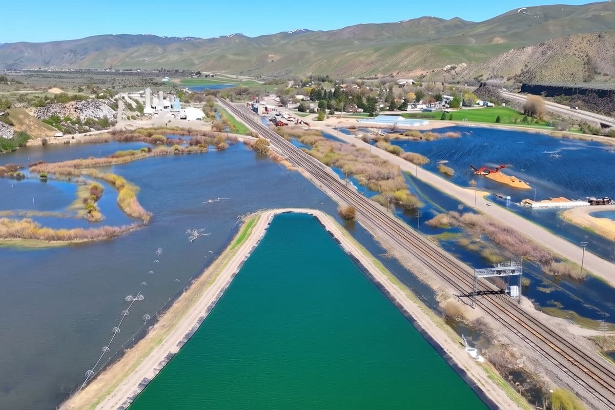 Die Lagunenkammern von Inkom, Idaho, aus der Luft; eine Kammer wird belüftet, daneben Bahnstrecke und Zementwerk, dahinter die Portneuf-Bergkette.
