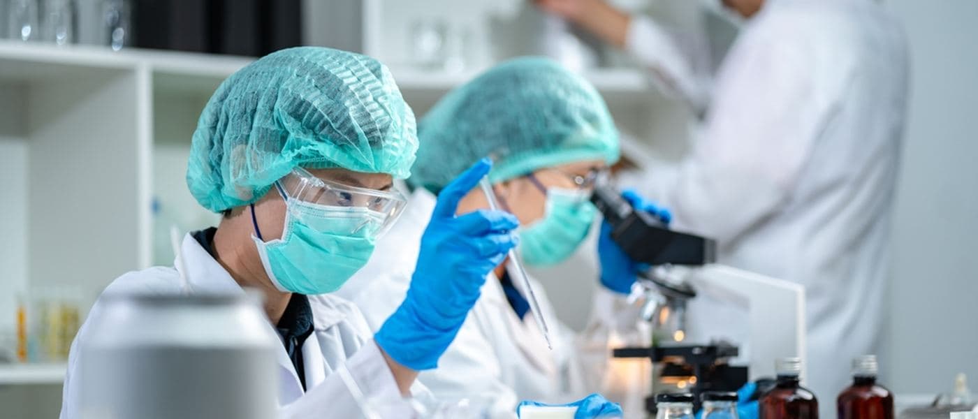 A laboratory team in protective clothing analysing samples at a bench of flasks and bottles.