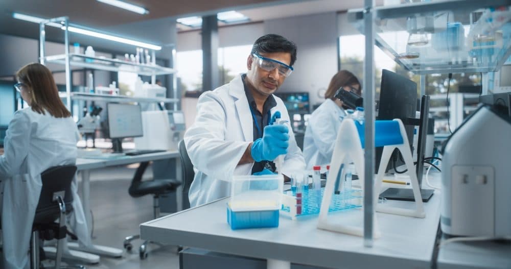 A technician pipetting samples into tube racks in an analytical microbiology laboratory.