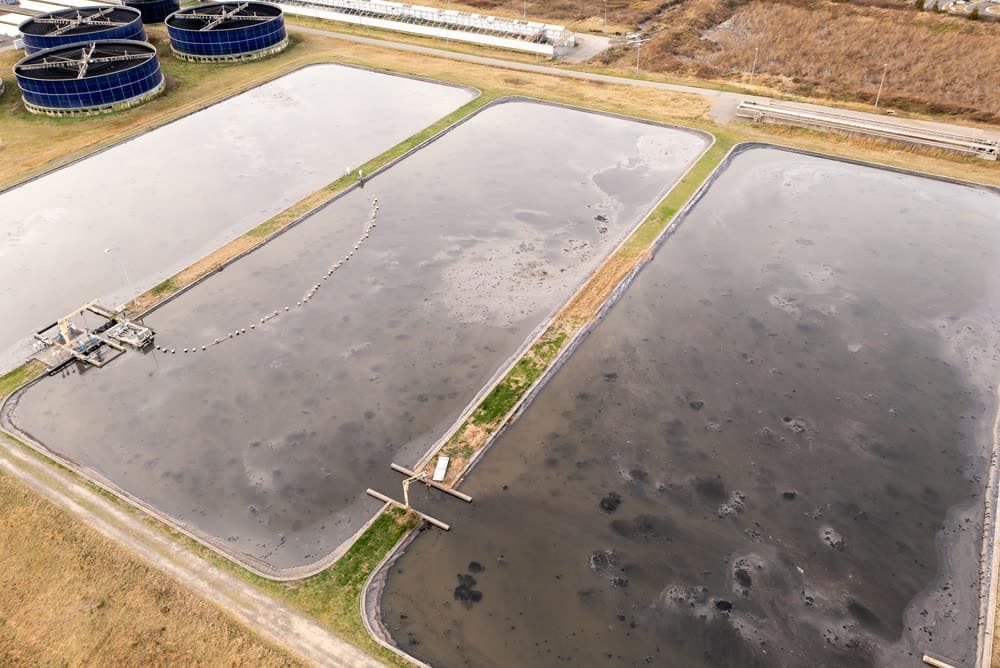Aerial view of a wastewater treatment lagoon and the adjacent clarifier tanks.